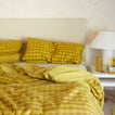 Bed with mustard bedding in solid and gingham with nightstand.