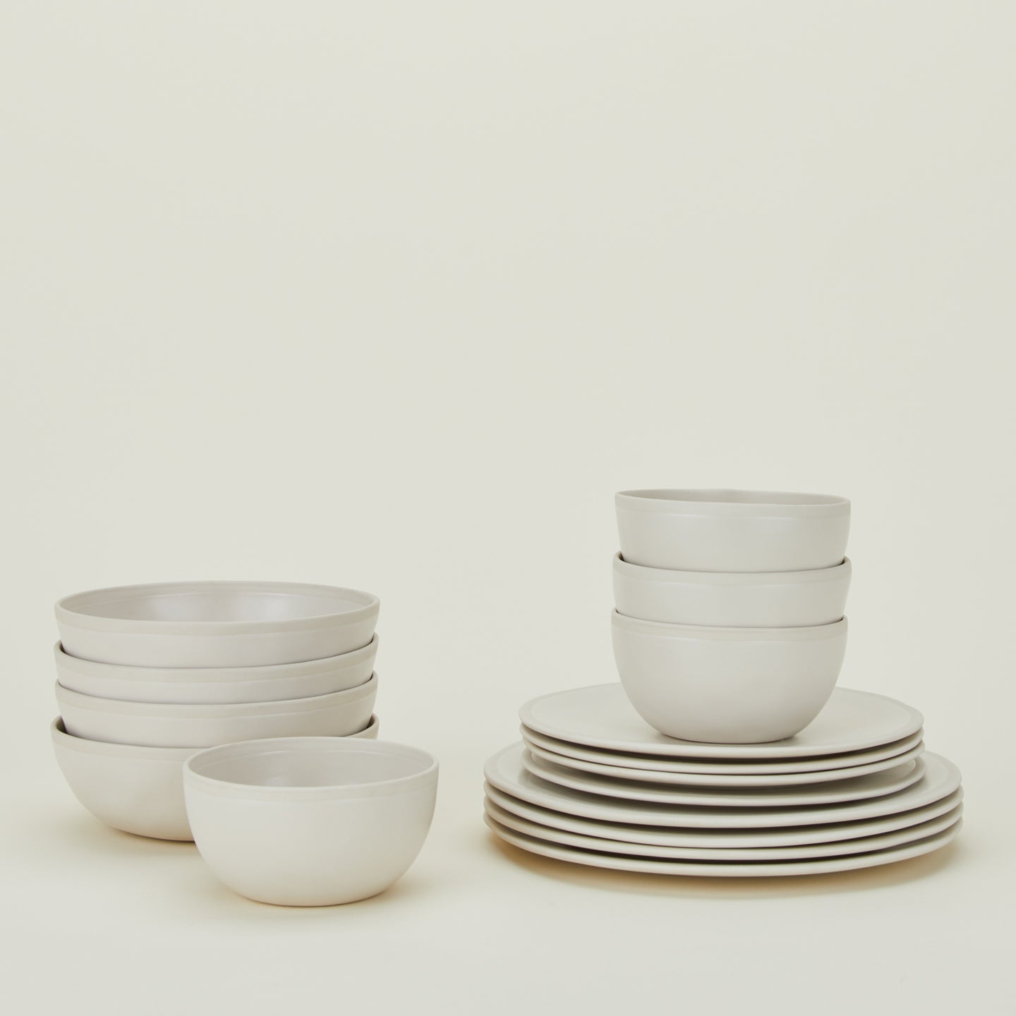 A neatly stacked set of white dinnerware includes plates, bowls, and small bowls against a plain background.