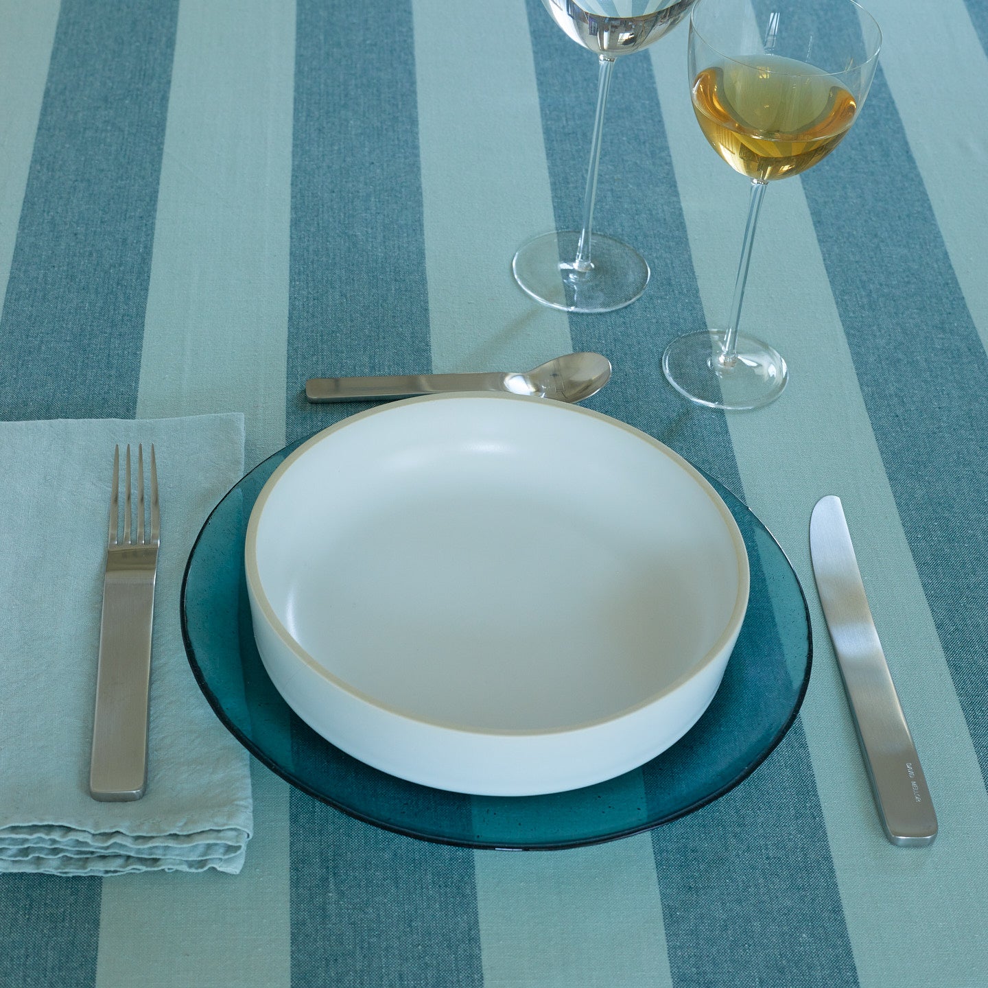 Placesetting with Glass Dinner Plate in Peacock on blue striped tablecloth.