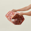 Hands unfolding collapsible marbled hexagon wastebasket.