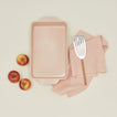 9" x 13" in essential bakeware in blush with apples, spatula, and dish towel