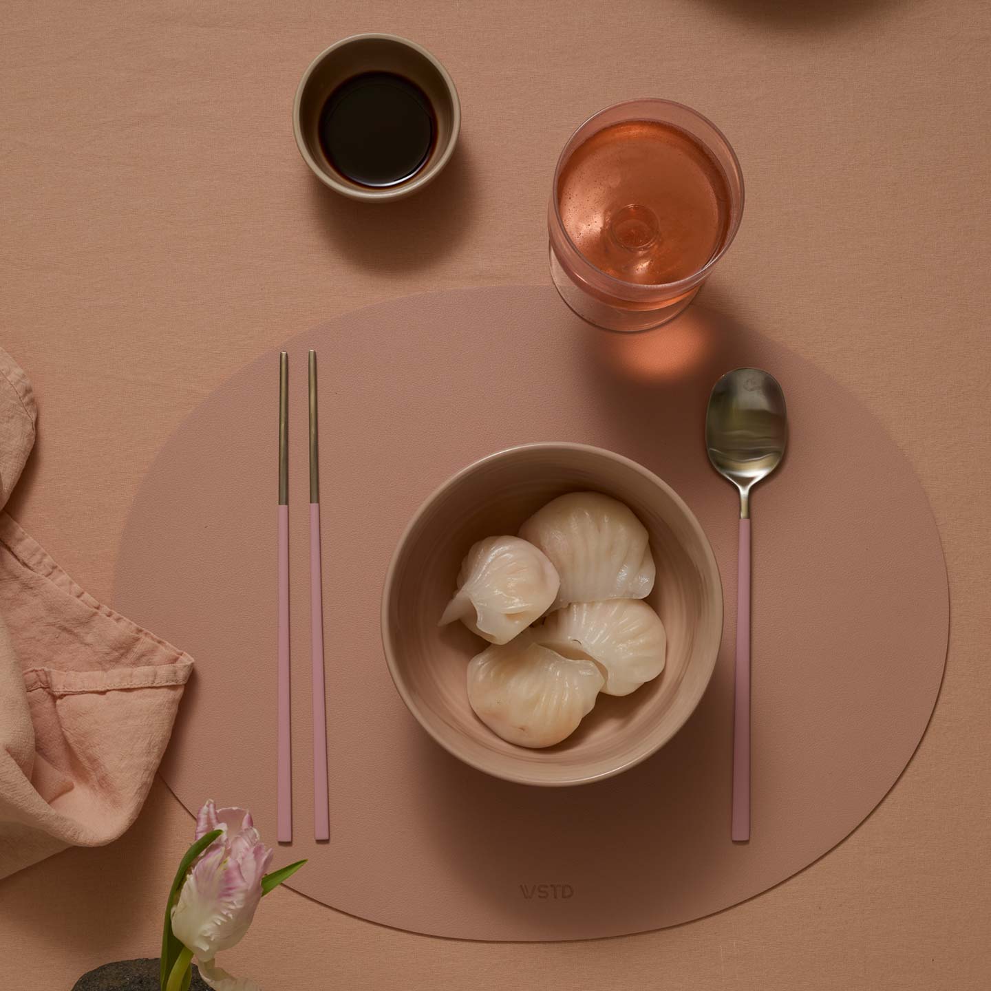 Dinner setting with a bowl of dumplings, a glass of pink drink, a cup of black coffee, and cutlery on a pink placemat.