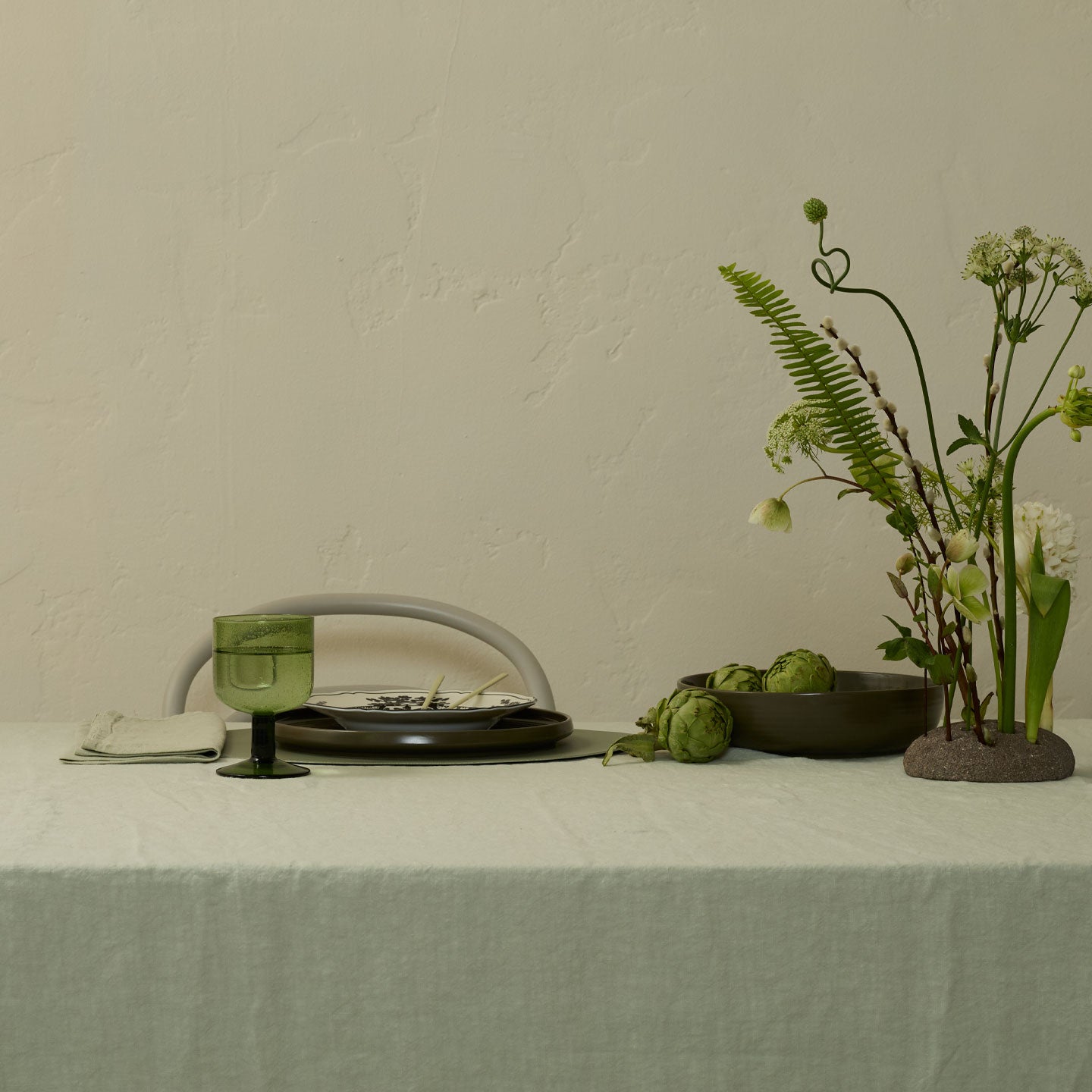Table setting with a glass, bowl, and decorative plants on a neutral background