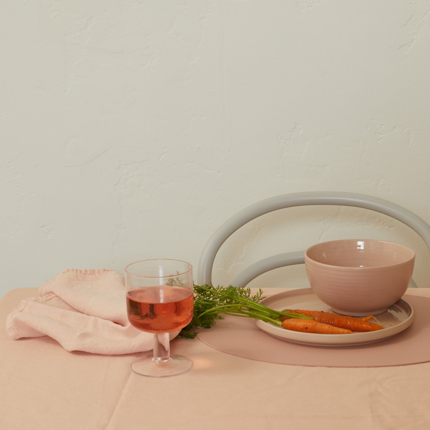 Glass of pink drink with carrots and a bowl on a beige surface