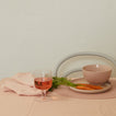 Glass of pink drink with carrots and a bowl on a beige surface