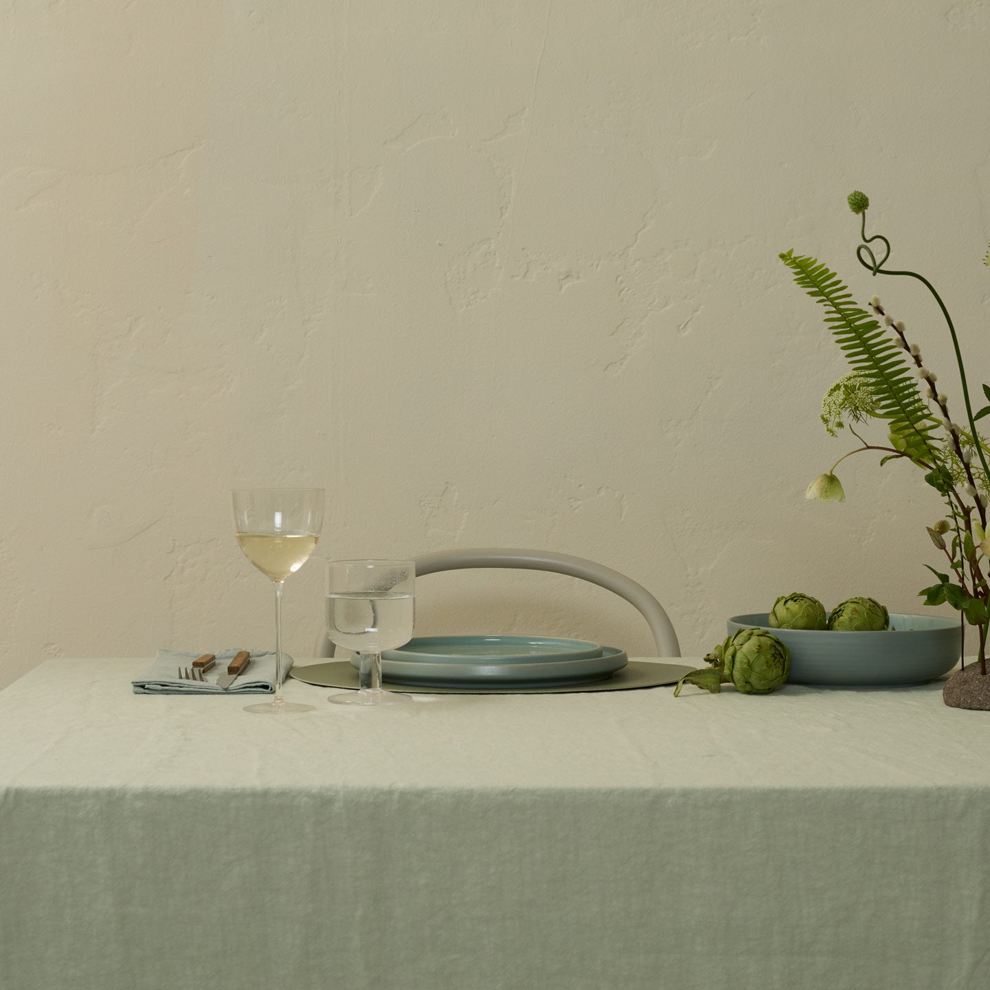 Table setting with a glass of white wine, plates, and a plant on a neutral background