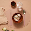Dinner setting with a bowl of dumplings, chopsticks, a spoon, and a glass on a pink placemat.