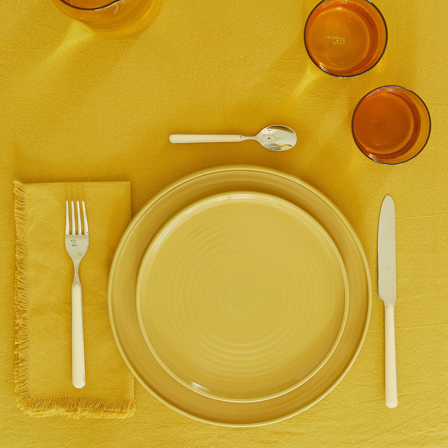 Placesetting with Essential Dinner Plate in Mustard on yellow tablecloth.