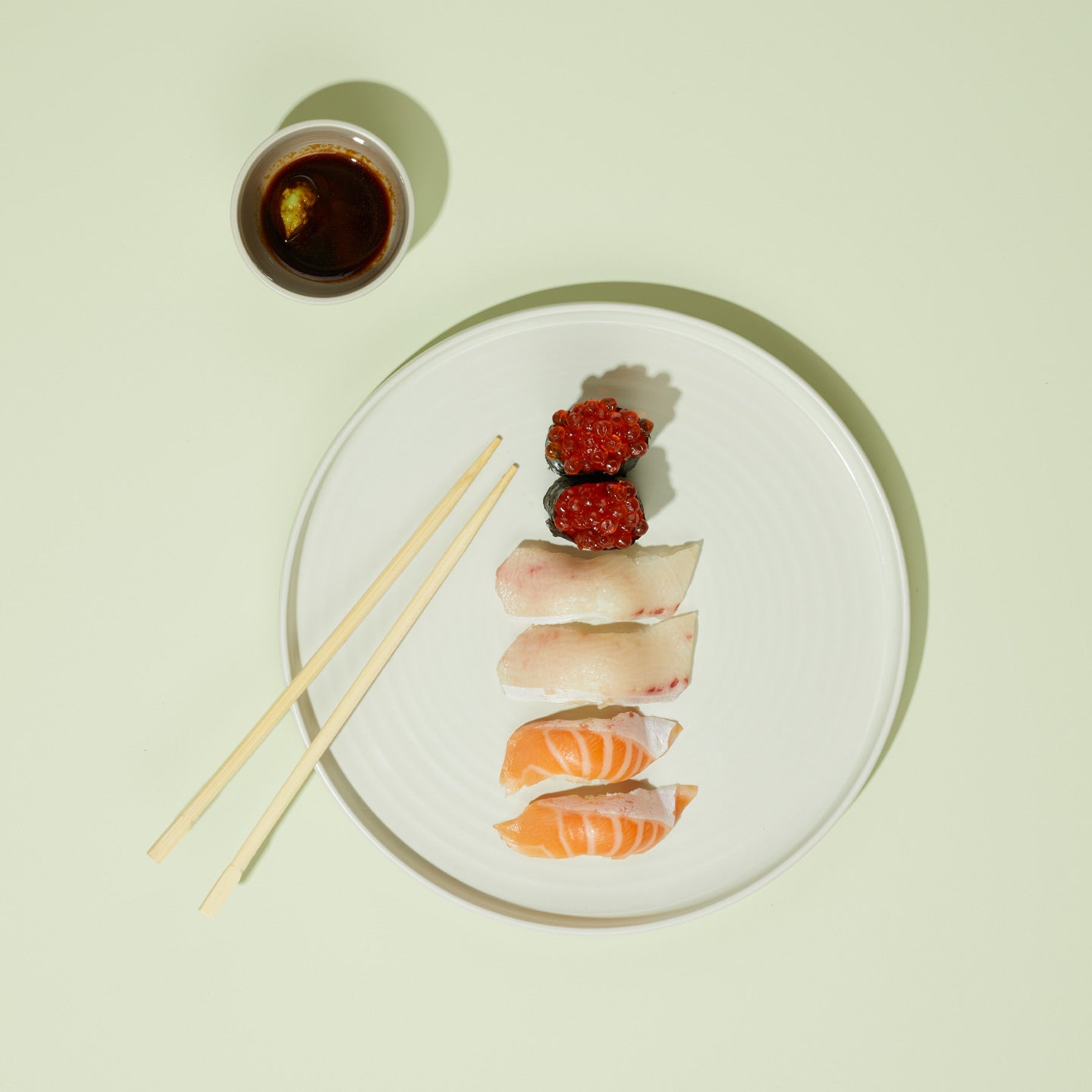 Sushi plate with sushi, wasabi, and soy sauce on a light green background