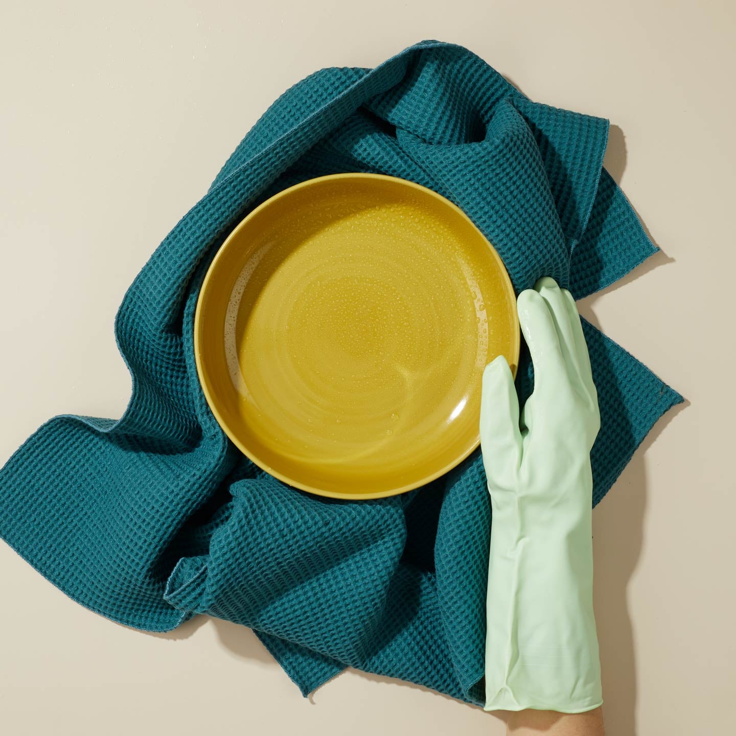 Yellow pasta bowl on a peacock essential towel with a green cleaning glove