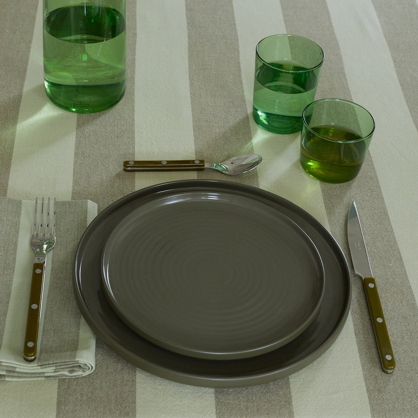 Placesetting with Essential Glassware in Green on green striped tablecloth.