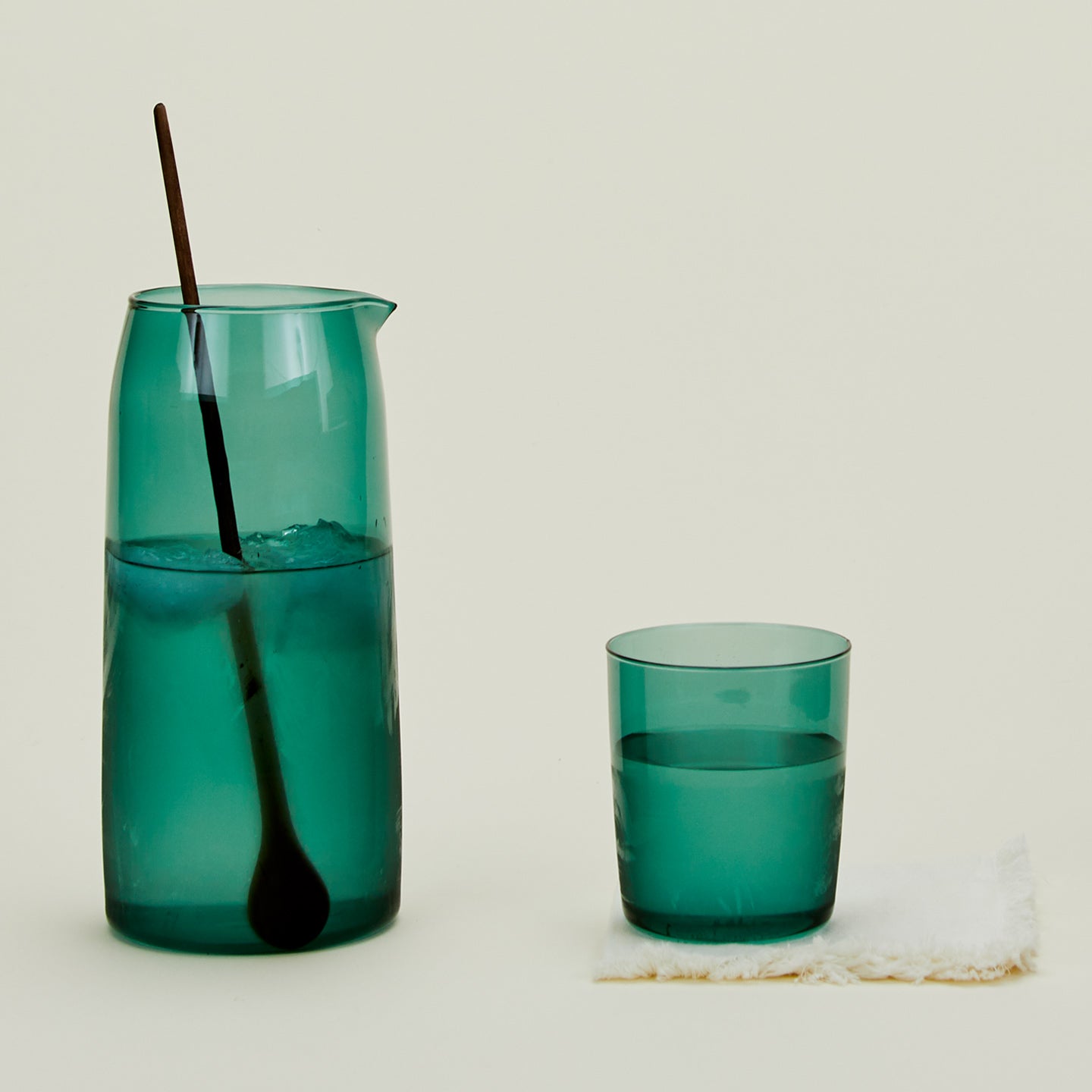 Essential Glassware Pitcher in Peacock, filled with ice water, along with a drinking glass and stirring spoon.