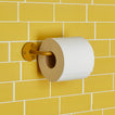 Essential toilet paper holder in Mustard with a roll of toilet paper on tiled wall.