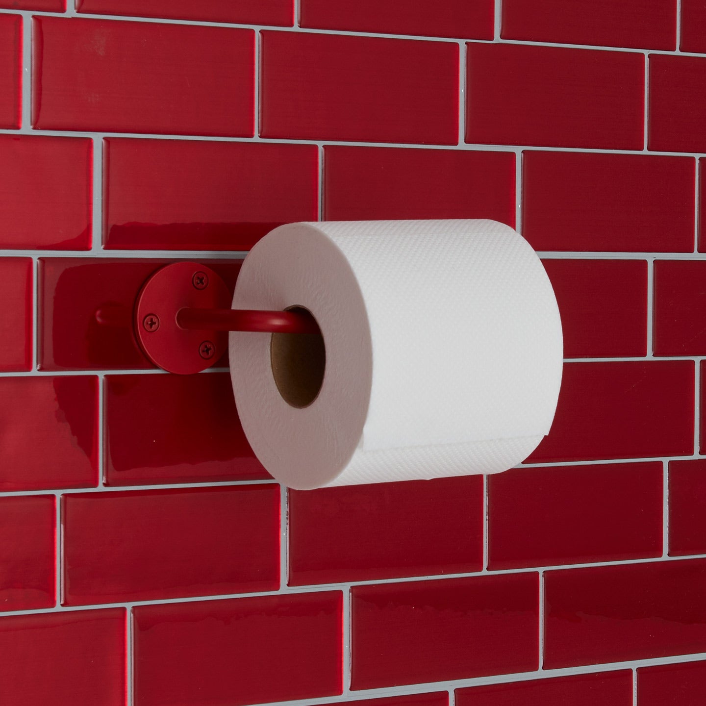 Essential toilet paper holder in red on tile background.