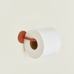 Toilet paper holder in Terracotta with a roll of toilet paper.
