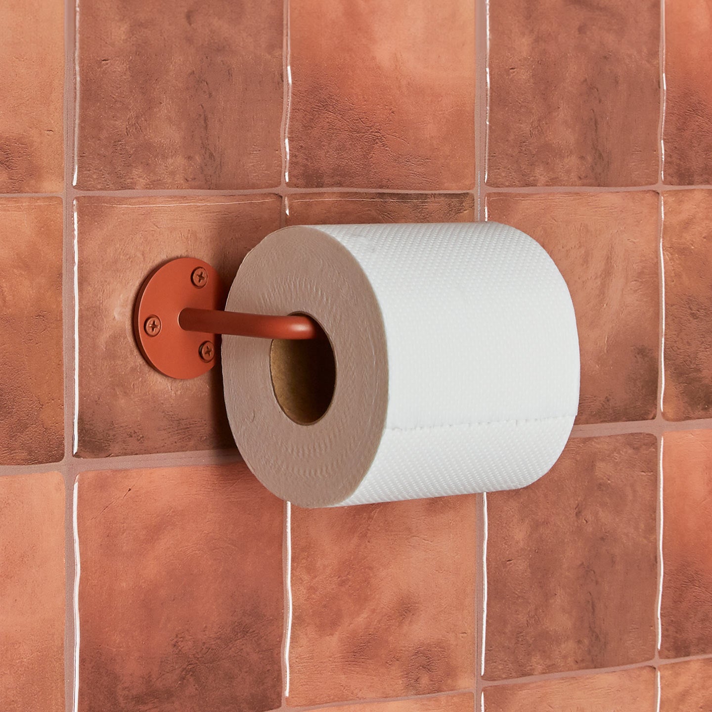 Essential toilet paper holder in Terracotta with a roll of toilet paper on tiled wall.