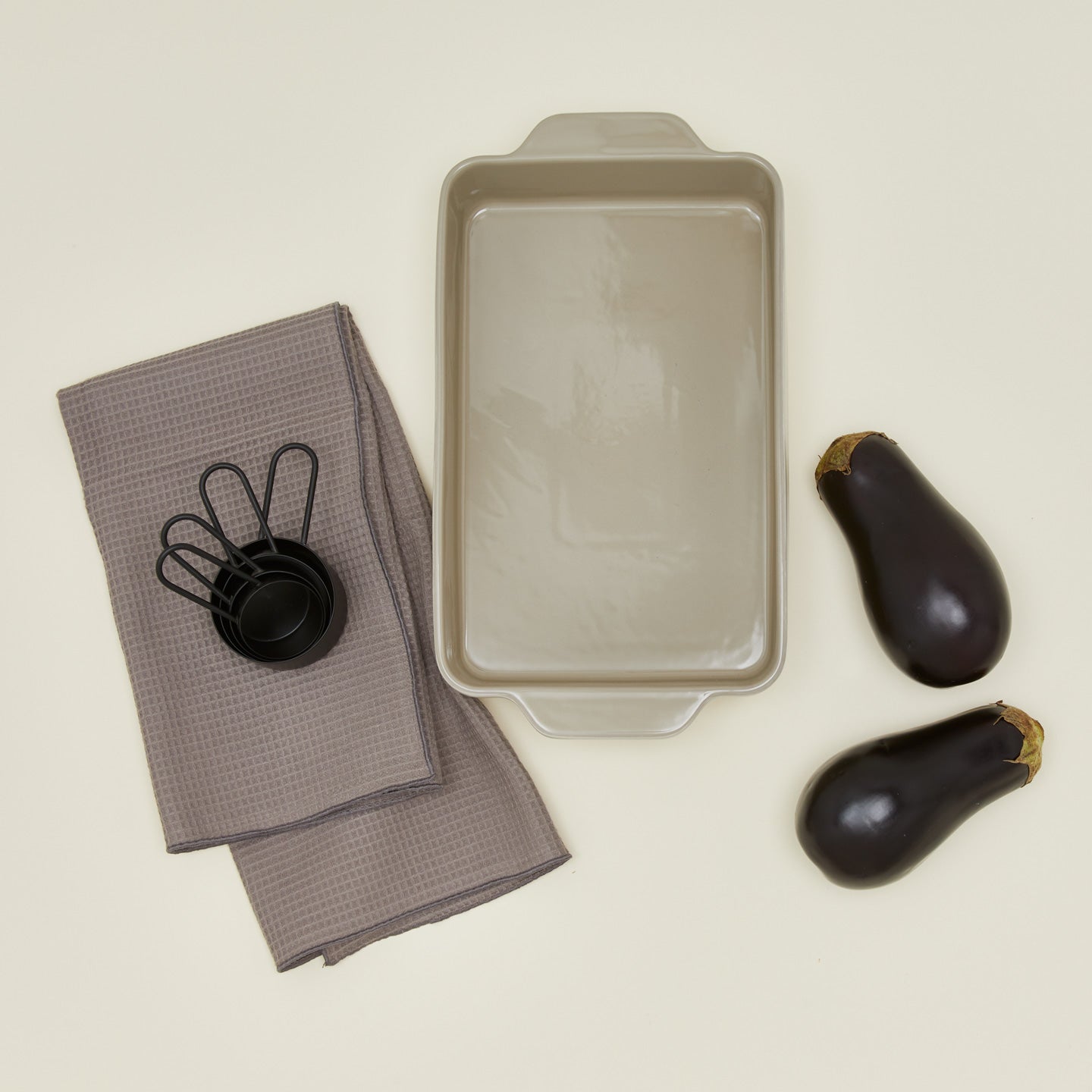 9x13 bakeware in light grey with eggplants, dishtowel and measuring cups