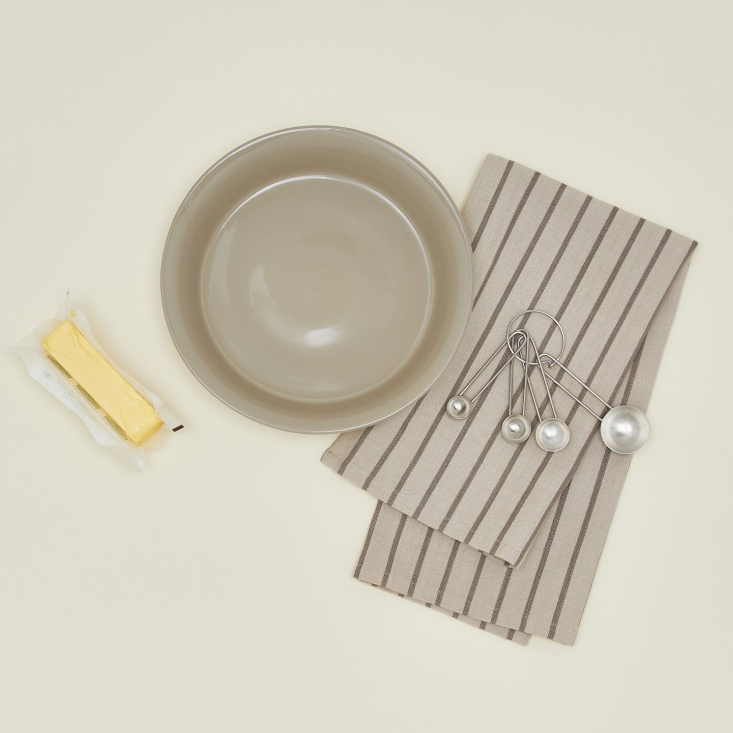 Essential pie dish in light grey with measuring spoons, butter, and dish towel