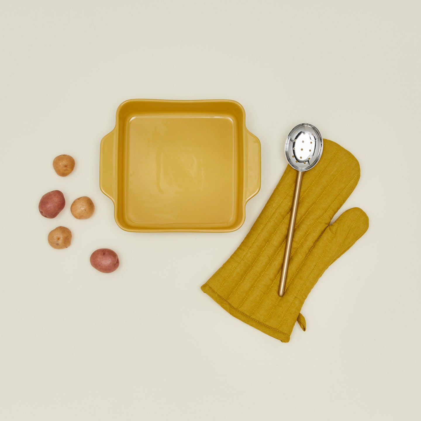 8x8 bakeware in mustard with potatoes, oven mitt and spoon