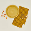 Pie dish in mustard with cherry tomatoes dish towel and measuring spoons