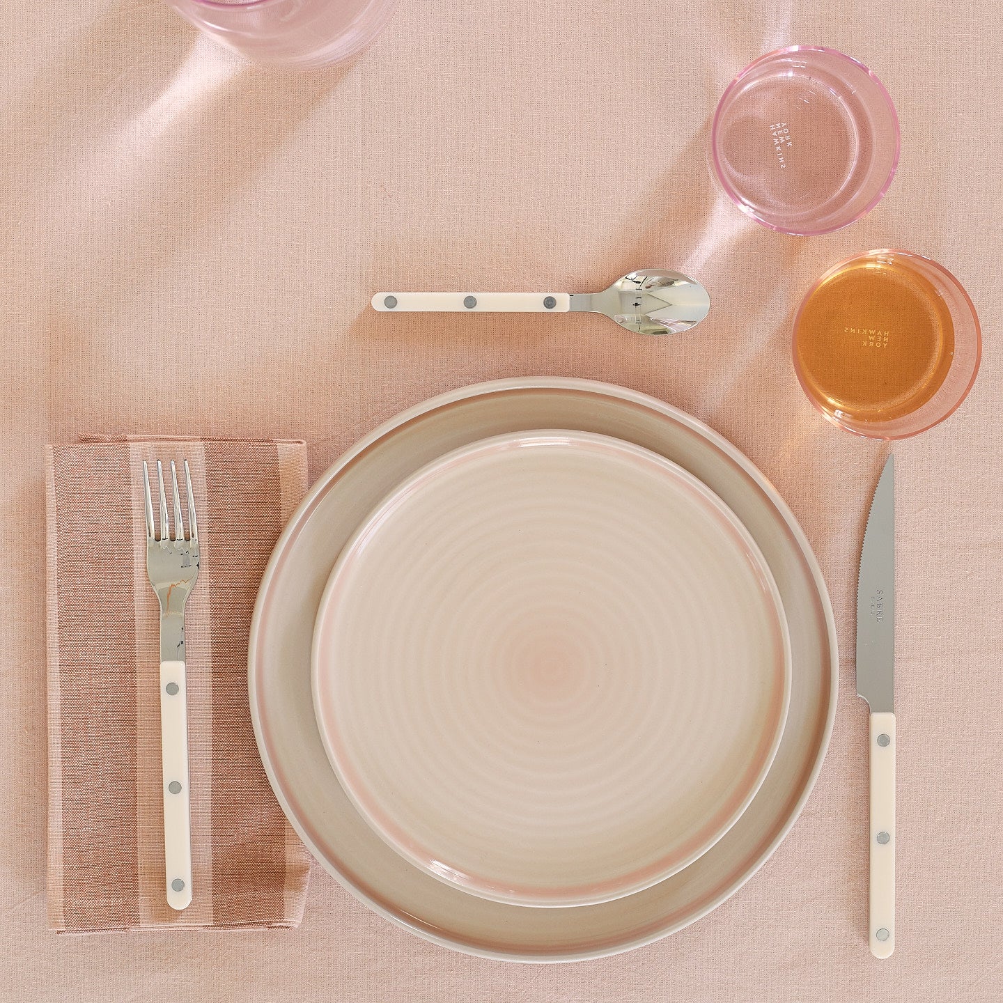 Placesetting with Essential Striped Dinner Napkin in Blush and Terracotta on pink tablecloth.
