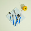 Blue flatware on folded Essential Dinner Napkin in Sky on light background with yellow pepper.