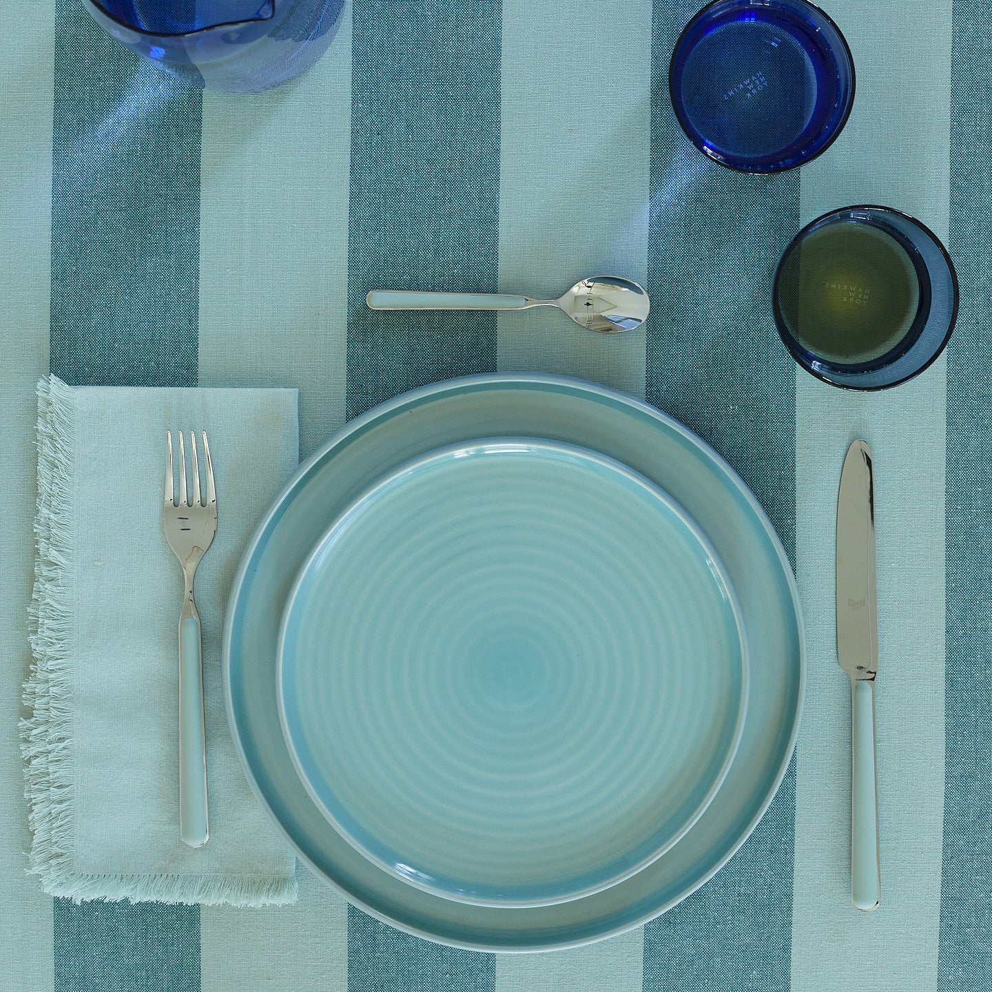 Placesetting with Essential Dinner Napkin in Sky on blue striped tablecloth.