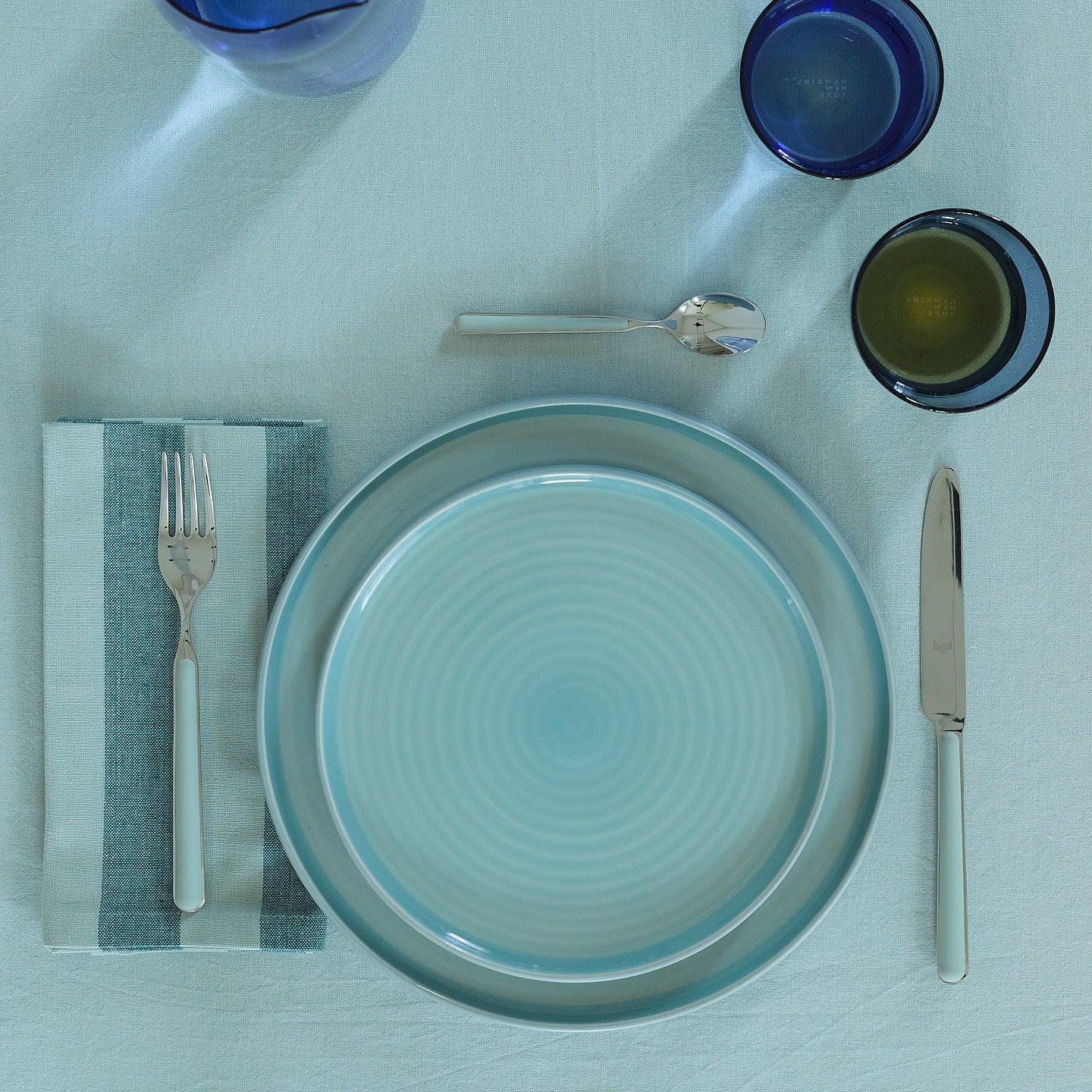Placesetting with Essential Striped Dinner Napkin in Sky and Peacock on blue tablecloth.