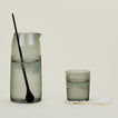 Essential Glassware Pitcher in Smoke, filled with ice water, along with a drinking glass and stirring spoon.