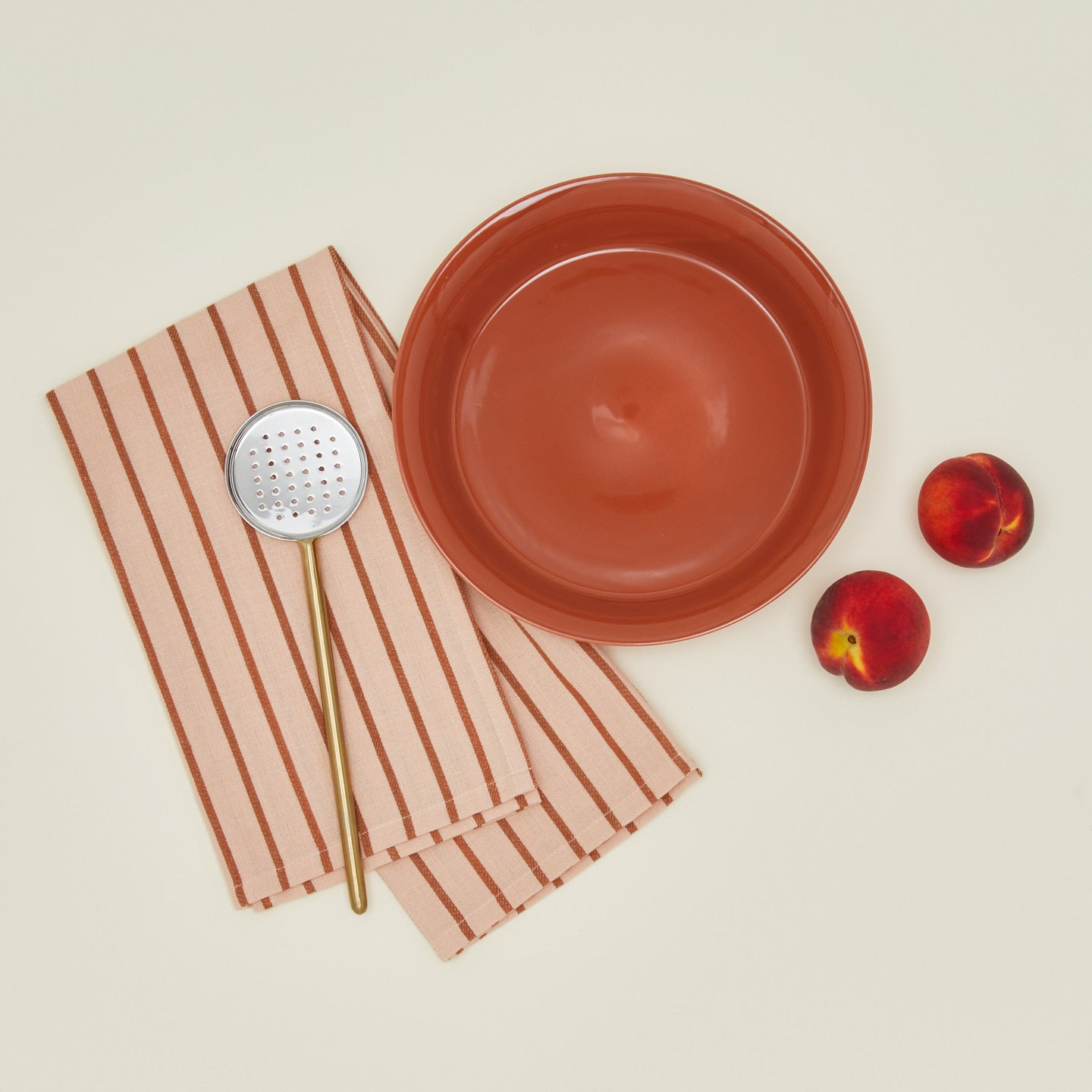 Pie dish in terracotta with peaches dishtowel and slotted spoon