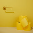 Three rolls of yellow toilet paper on a beige surface with a yellow wall background and mustard toilet paper holder.