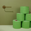 Stack of green toilet paper rolls against a green wall with an olive toilet paper holder.