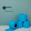 Stack of blue toilet paper rolls on a light blue surface with a teal wall and Essential Peacock toilet paper holder in the background.