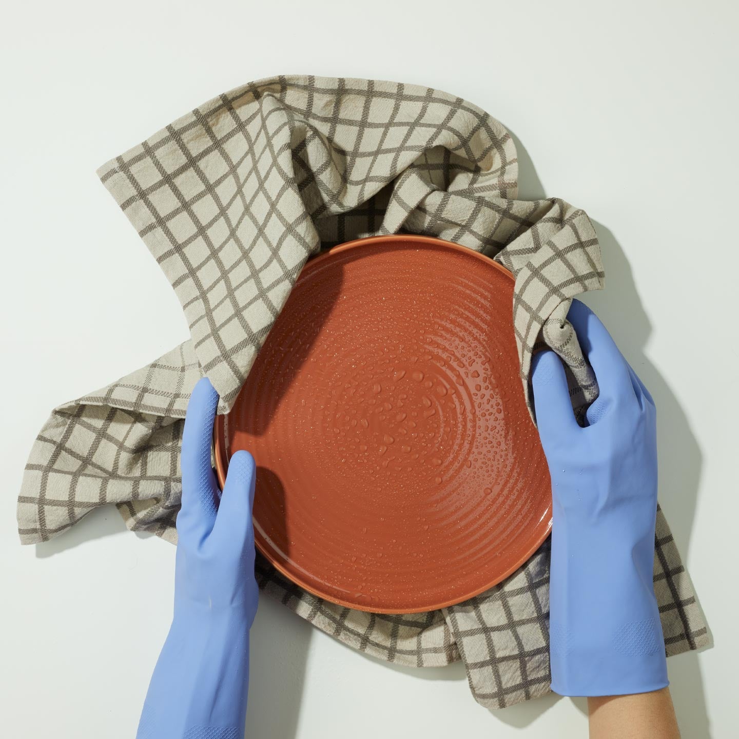 Hands wearing blue gloves holding wet terracotta plate in Essential Yarn Dyed Dishtowel in Grey on white background.