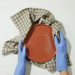 Hands wearing blue gloves holding wet terracotta plate in Essential Yarn Dyed Dishtowel in Grey on white background.