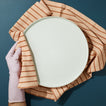 White plate held by a gloved hand on an Essential striped towel in blush against a blue background