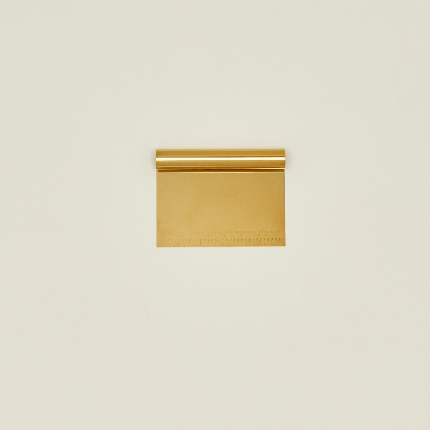 Brass dough scraper on a beige background.