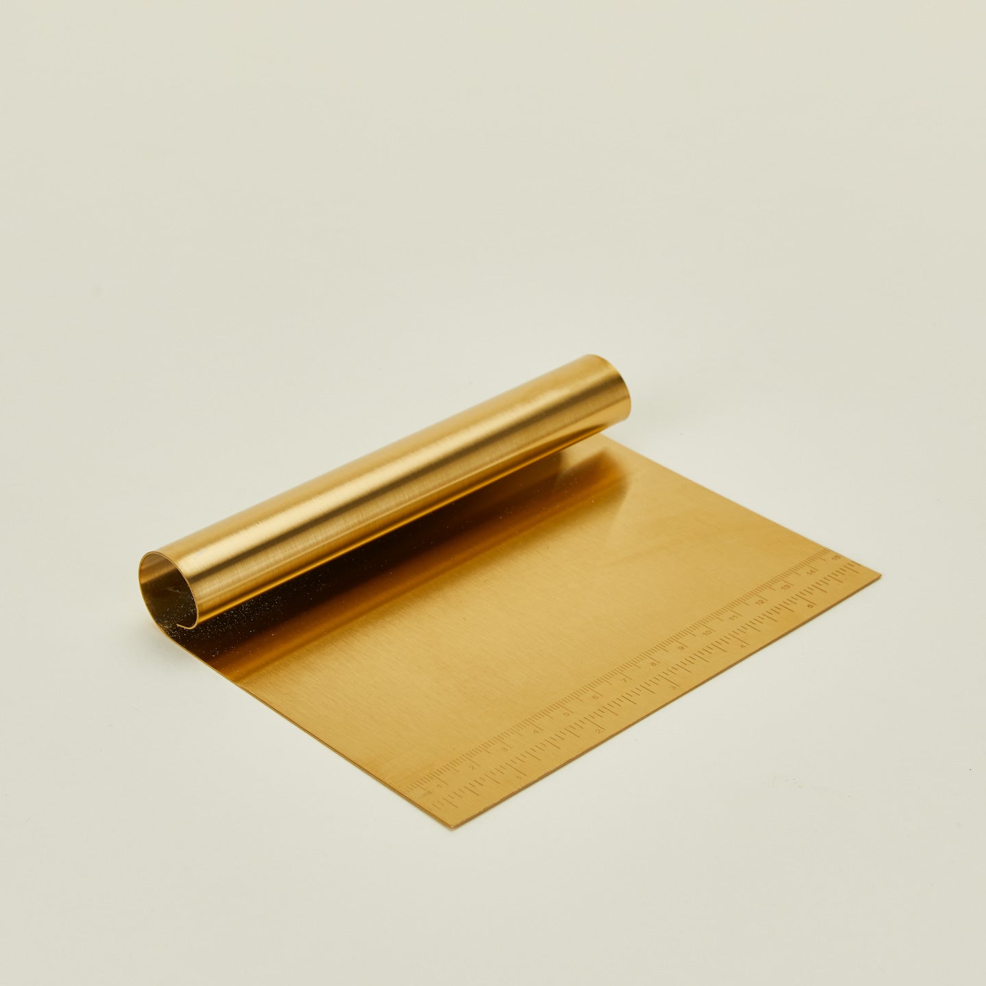 Close up of Brass dough scraper on a beige background.