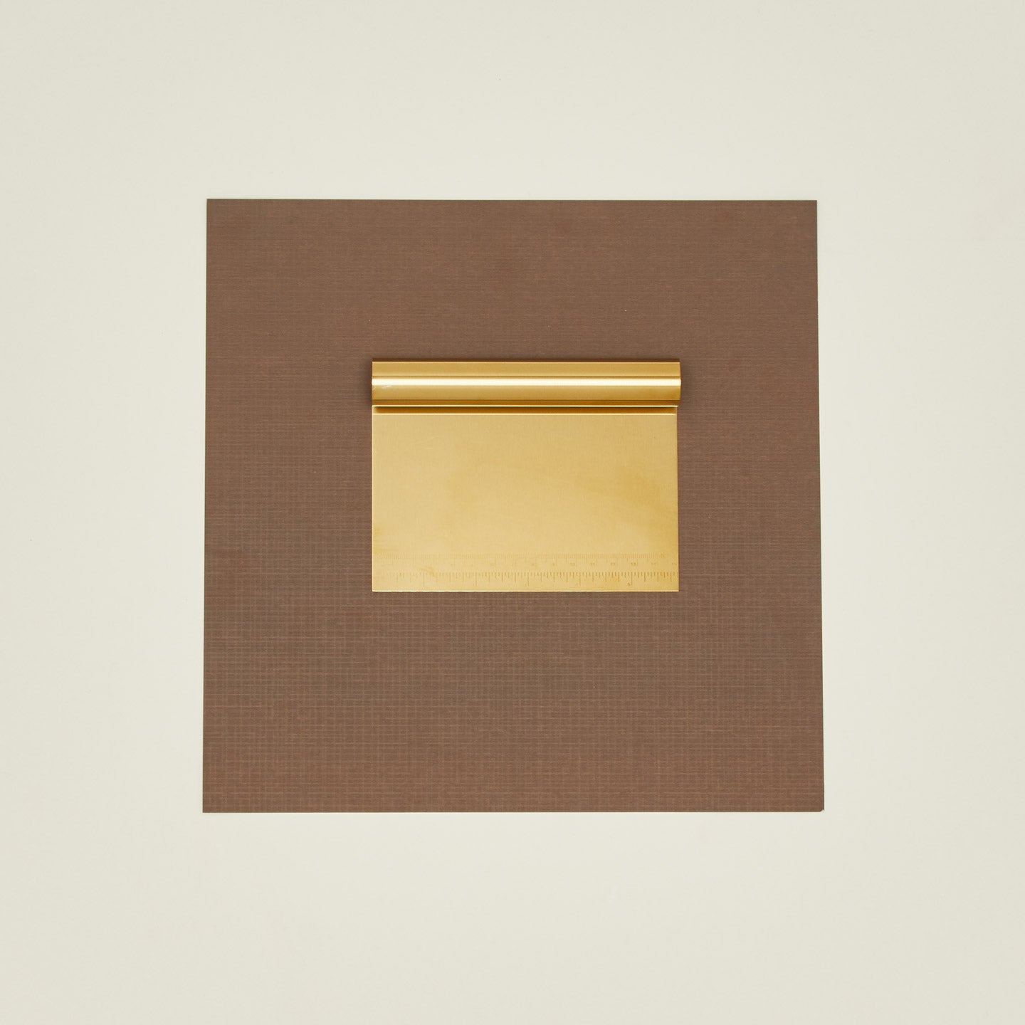 Brass dough scraper on a brown paper on a beige background.