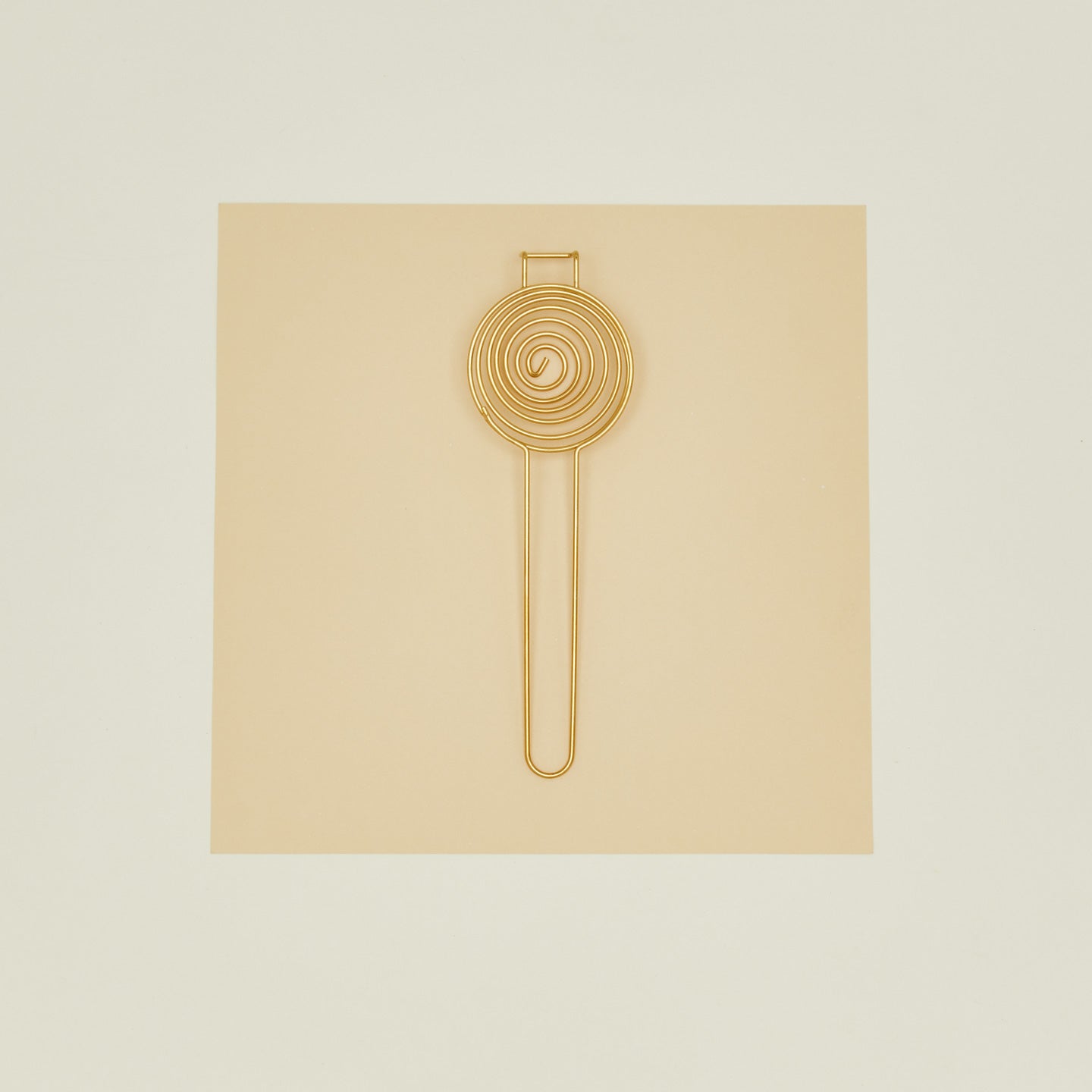 Brass swirl egg separator on beige paper on ivory background.
