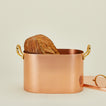 Open copper bread box with load of bread and lid on ivory background.