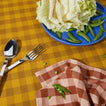 Essential Gingham napkin in Blush on Essential Gingham tablecloth in Mustard with Serving Set and blue plate with peas and greens.