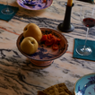 Marble table set with wine glasses, cloth napkins, candlelight and Ginori porcleain pieces with floral motifs and gold accents.