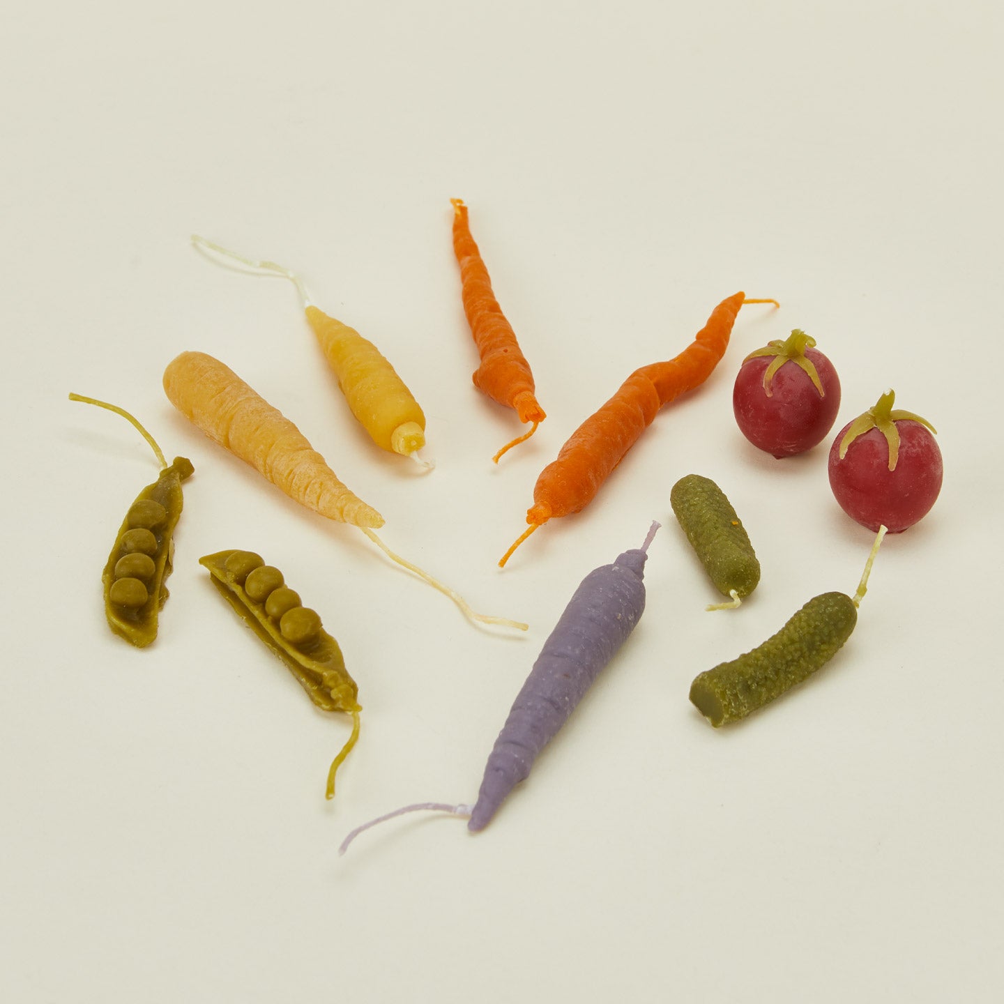 Colorful vegetable candles including carrots, peas, and radishes on a light background