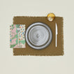 A table setting with olive plates, an amber glass, an olive placemat, and a fern patterned napkin.