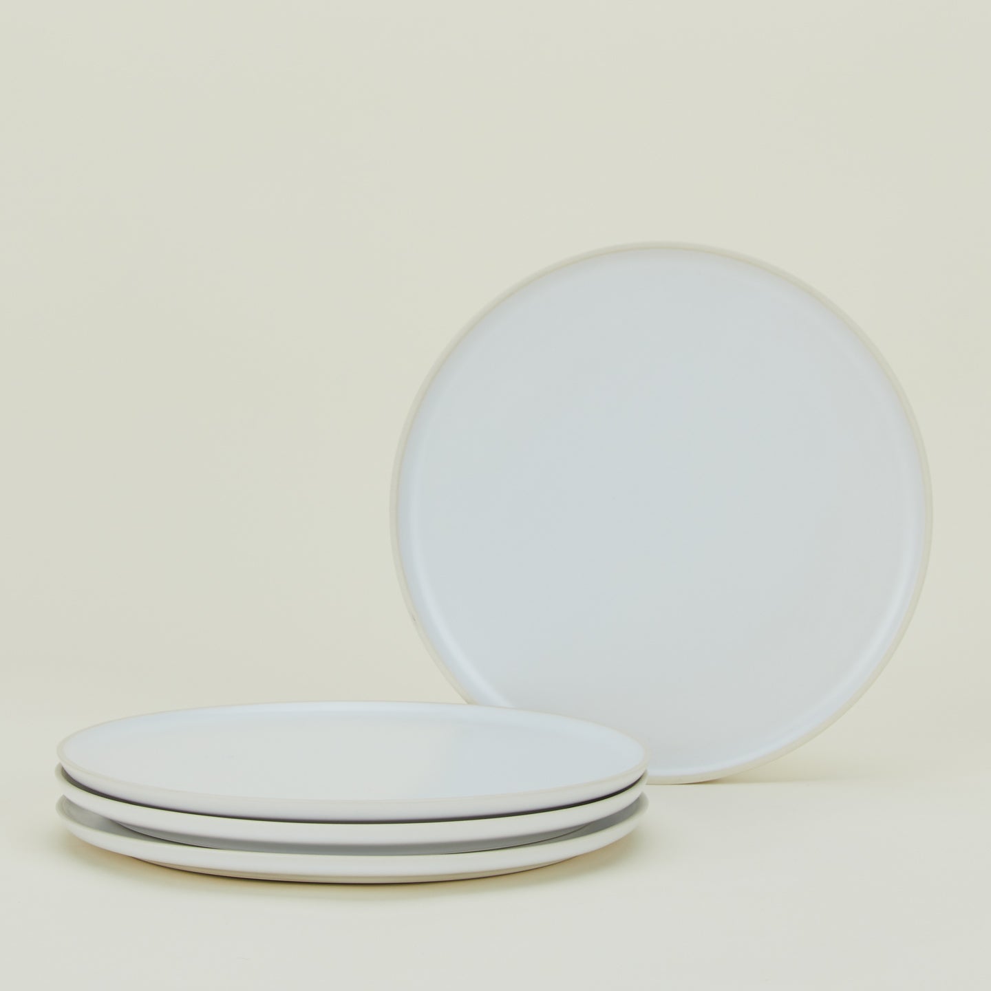 Four stackable white plates on a pale background. One plate stands upright, while the other three are stacked horizontally.
