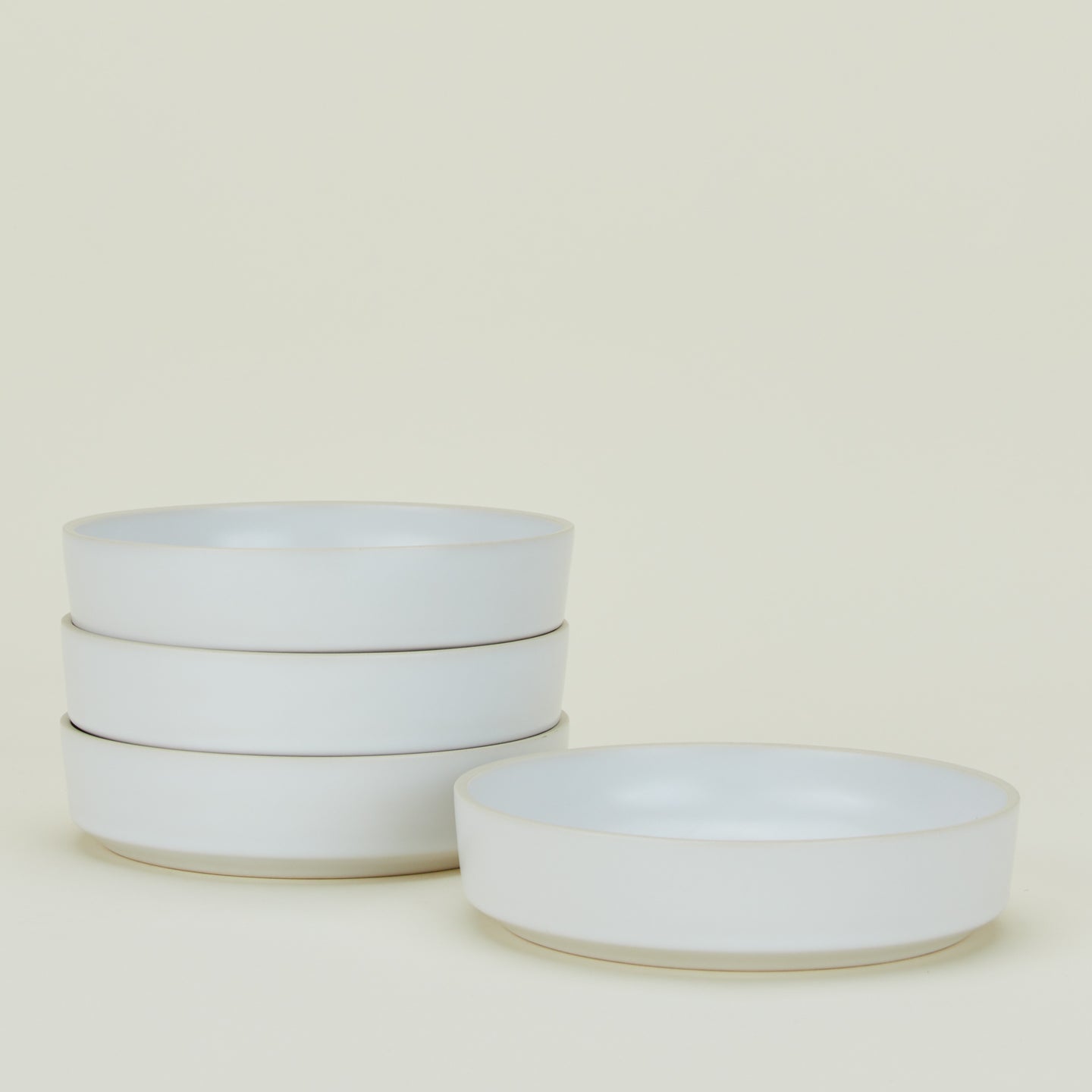 A set of four white ceramic bowls stacked in a column except for one, which is lying adjacent.