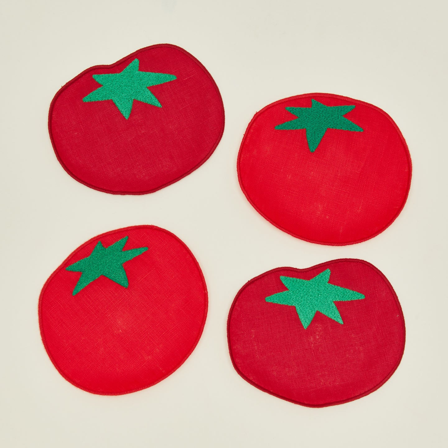 Close up of four red tomato-shaped coasters with green stems on a beige background