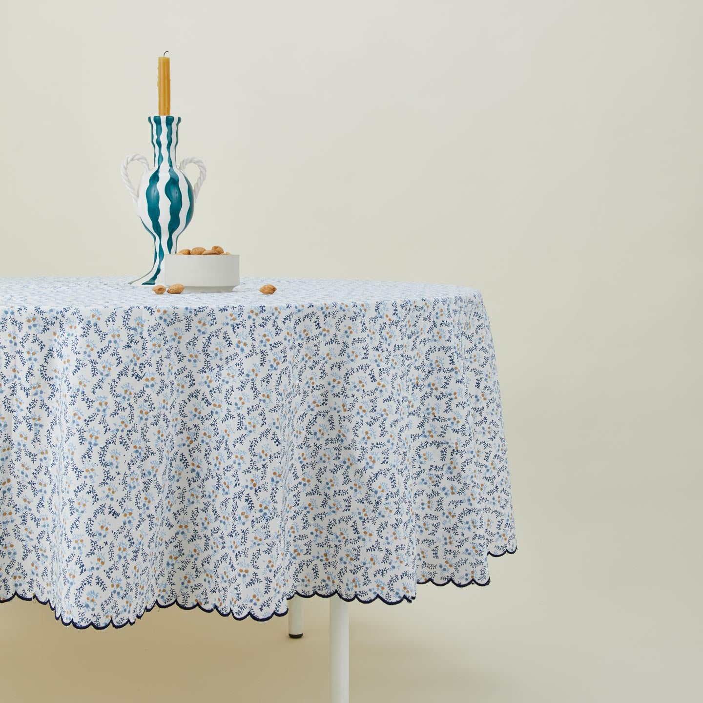 Little flowers round tablecloth in blue on table with candle in candleholder and bowl with almonds.