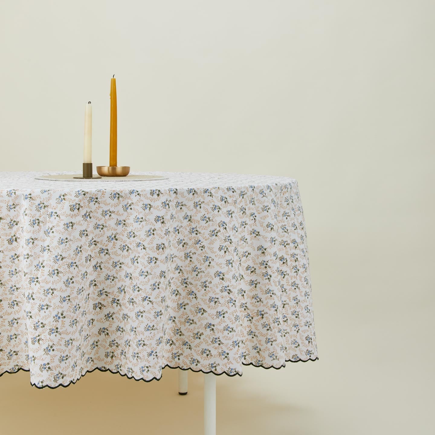 Little flowers round tablecloth in green on table with candles in candleholders.